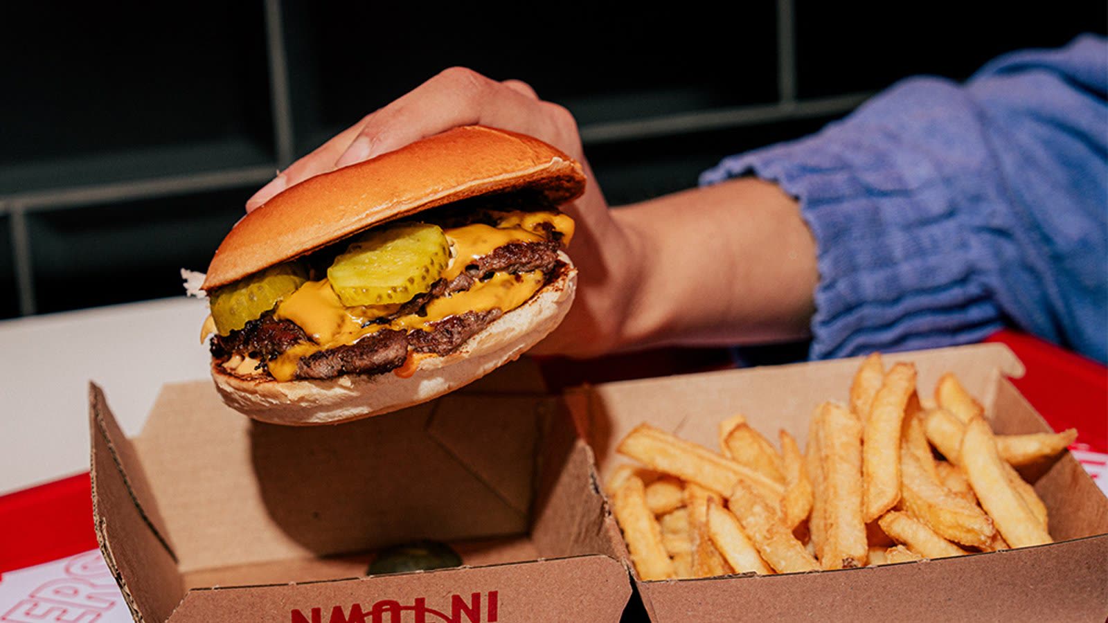 Een dubbele cheeseburger van Johnny's met augurk en burgersaus, naast een bakje friet.